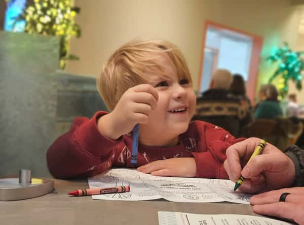 A happy child enjoying a meal and coloring at a restaurant table.