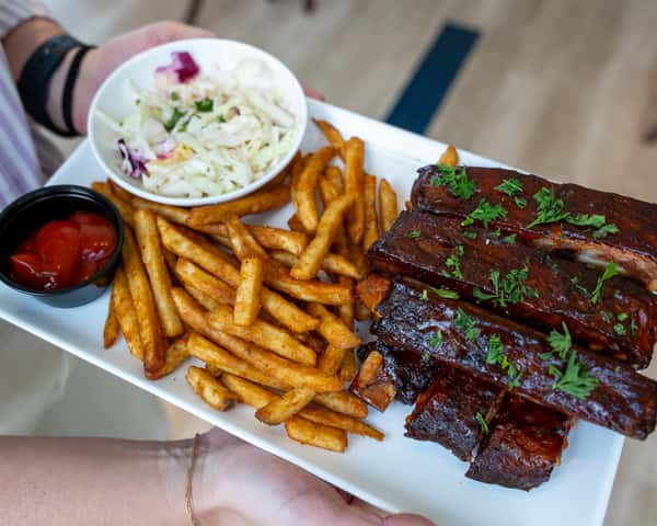 Plate of ribs served with fries and dipping sauces.