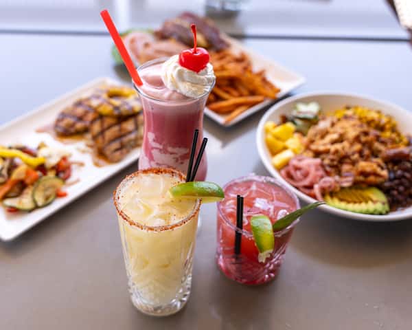 Table scene with colorful drinks and plated food in the background.