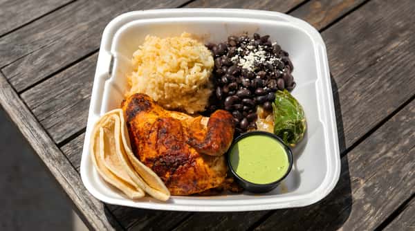 Peruvian-style chicken plate with rice, beans, tortillas, and green sauce.