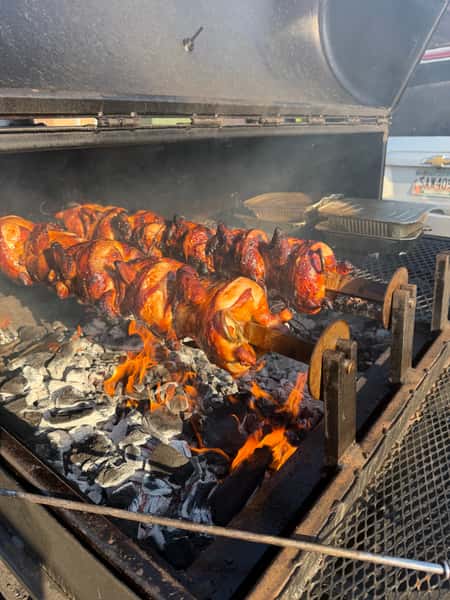 Whole chickens roasting on a rotisserie over open flames.