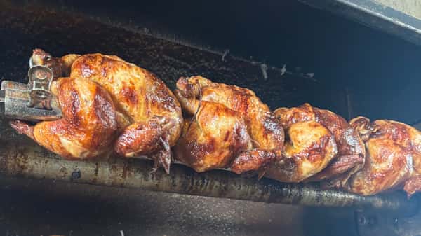 Whole roasted chicken cooking on a rotisserie over open flame.