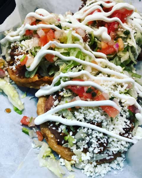 Handmade sopes layered with refried beans, shredded lettuce, diced tomatoes, cotija cheese, and drizzled with Mexican crema—served fresh for a hearty and traditional antojito.