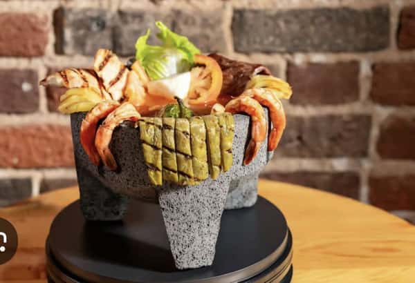 Traditional Mexican molcajete platter filled with grilled shrimp, steak, chicken, cactus (nopal), and fresh vegetables—served sizzling in a stone mortar for a bold and authentic presentation of surf and turf Mexican cuisine.