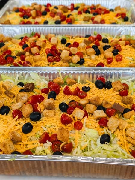 Fresh catering house salads topped with shredded cheddar cheese, cherry tomatoes, black olives, seasoned croutons, and crisp iceberg lettuce.