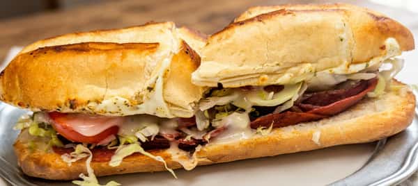 Toasted Italian sub sandwich loaded with salami, ham, pepperoni, melted mozzarella, lettuce, tomato, and Italian dressing on a fresh baked roll.