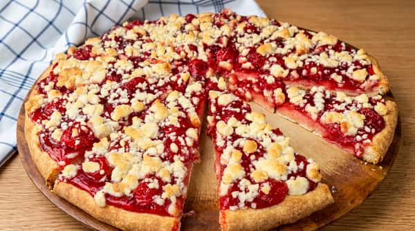Cherry crumb pie topped with golden streusel and sliced on a wooden serving board