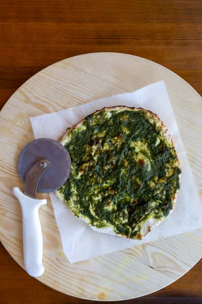 A flatbread topped with spinach and cheese, accompanied by a pizza cutter on a wooden platter.