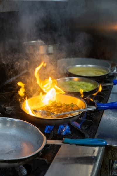 A close-up of a stovetop with multiple pans, one emitting flames during the cooking process.