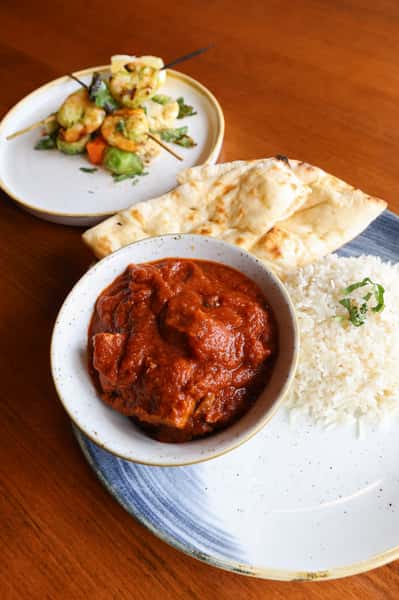 A bowl of Indian curry with naan bread and rice on a plate.