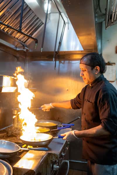 A chef cooking in a kitchen, with flames erupting from a stovetop.