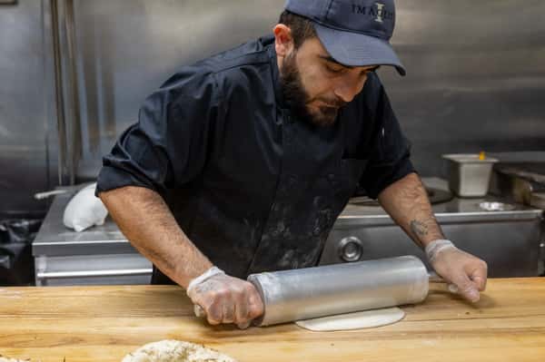 A chef rolling dough with a rolling pin, focused on preparing food in a kitchen setting.