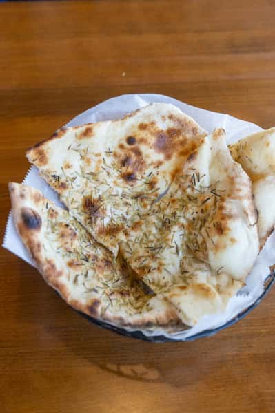 A basket of freshly baked naan bread, topped with herbs and served on a round plate.