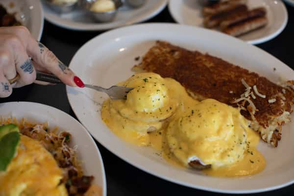 Creamy eggs Benedict topped with silky hollandaise sauce and garnished with herbs, served alongside crispy golden hash browns at a cozy American breakfast diner — a popular brunch favorite.