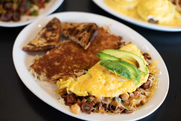 Southwestern omelette stuffed with diced vegetables and cheddar cheese, topped with sliced avocado, served with crispy hash browns and grilled flatbread — a colorful and filling breakfast dish.