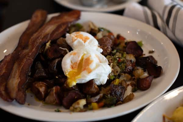 Hearty breakfast hash with roasted potatoes, bell peppers, and onions, topped with two poached eggs and served with thick-cut crispy bacon — a savory and satisfying diner-style morning plate.