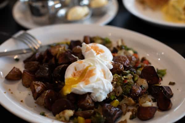 Savory breakfast hash made with roasted potatoes, diced vegetables, and herbs, topped with two perfectly poached eggs with runny yolks — a flavorful and rustic dish served at a farm-style American diner.