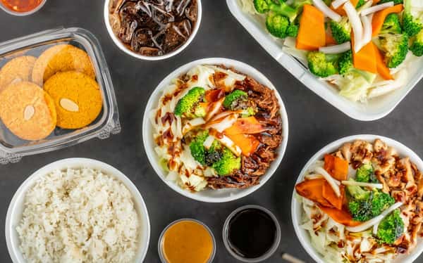Asian-style chicken and beef bowls with fresh vegetables, steamed rice, dipping sauces, and cookies
