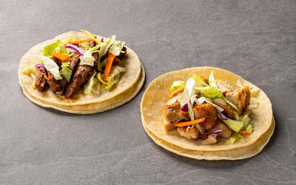 Beef and chicken tacos with lettuce, carrots, and red onion served on warm corn tortillas