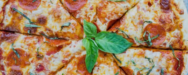 Cheesy pizza with tomato slices and a rocket leaf garnish