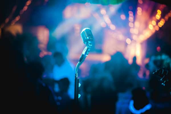 Vintage microphone on stage with blurred colorful lights and audience in the background.