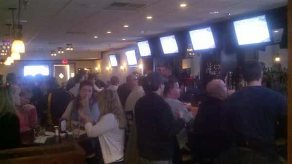 View of bar filled with people watching six TV screens behind bar.
