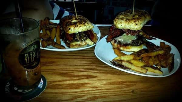 Two dishes with specialty burgers each one served with country fries and a glass of iced drink