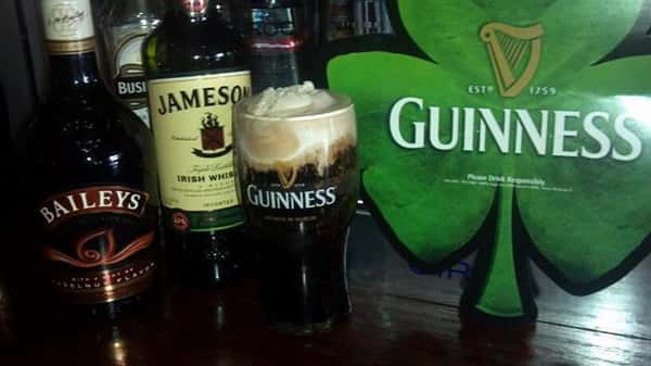 A glass of Guinness at the bar beside a bottle Baileys and a bottle of Jameson