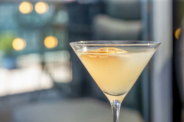 Martini garnished with a dried citrus wheel in a martini glass, with blurred string lights in the background at a restaurant