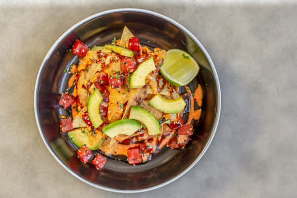 Tuna nachos with crispy chips, diced tuna, avocado, and tomatoes in a dark bowl, garnished with a lime wedge, on a table at a restaurant