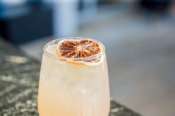 Pale pink cocktail garnished with a dried citrus wheel in a rocks glass, on an outdoor table at a restaurant