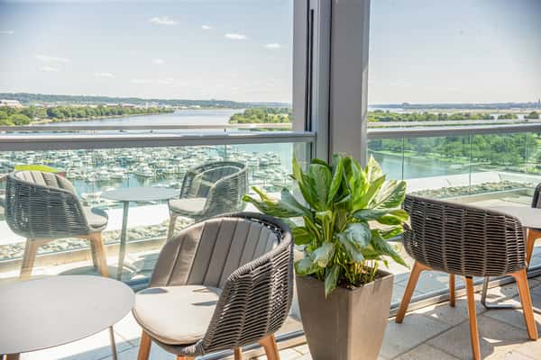 Rooftop patio seating area with woven chairs and a potted plant, overlooking a waterfront view at a restaurant