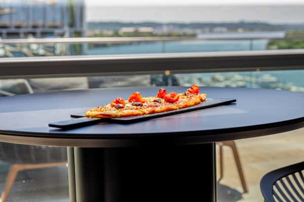 Mediterranean flatbread on a long black serving board on a dark table, with a waterfront view in the background at a restaurant