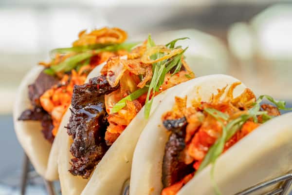 Close-up of brisket bao buns with pickled vegetables and scallions at a restaurant