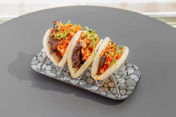 Brisket bao buns topped with fresh vegetables and herbs at Whiskey Charlie in Washington, DC