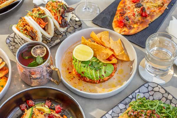Spread of restaurant dishes including guacamole with tortilla chips and lime, tacos, and flatbread on a table