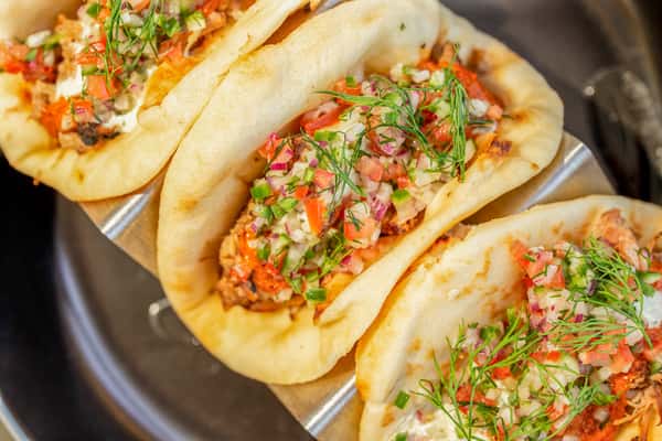 Lamb shawarma tacos with meat, herbs, and diced vegetables in soft shells, arranged in a row on a serving stand at a restaurant
