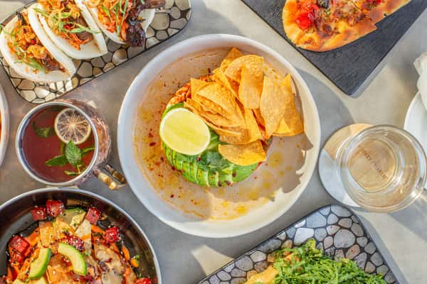 Overhead view of a spread of dishes including guacamole with tortilla chips and lime, tacos, hummus, and flatbread on a table at a restaurant