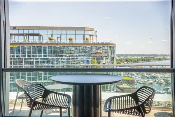 Rooftop patio seating area with a round dark table and woven chairs, overlooking a waterfront view at a restaurant