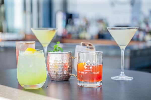 Lineup of assorted cocktails including martinis, a yellow citrus drink, a Moscow Mule in a copper mug, and an orange cocktail on a bar at a restaurant