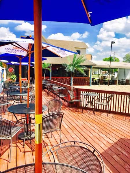 Outside deck with dining tables with umbrellas with a view of the beach volleyball court