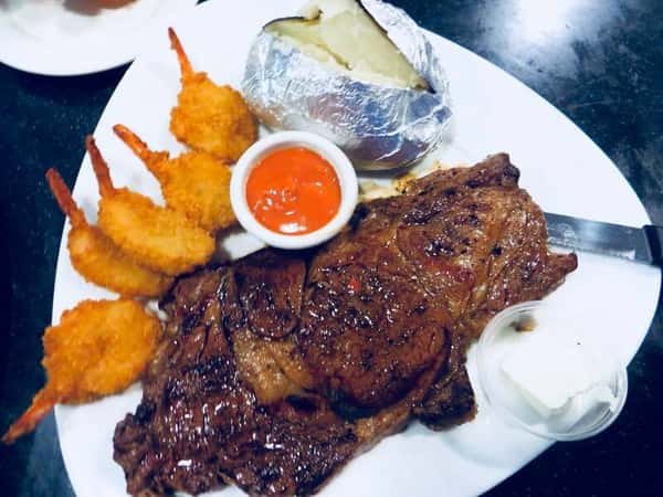 Grilled steak with a side of fried shrimp, baked potato and cocktail sauce