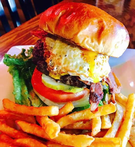 Burger with egg, pickle, tomato, onion, and lettuce with a side of fries