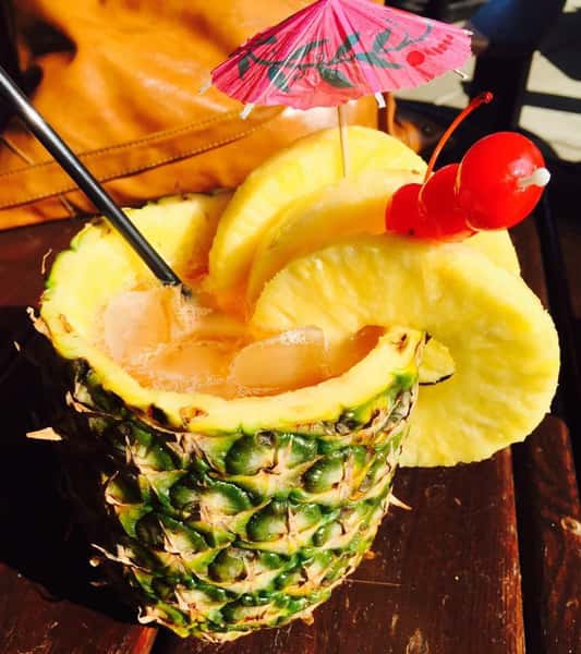 Tropical cocktail inside a real pineapple with slices of pineapple hanging out the side