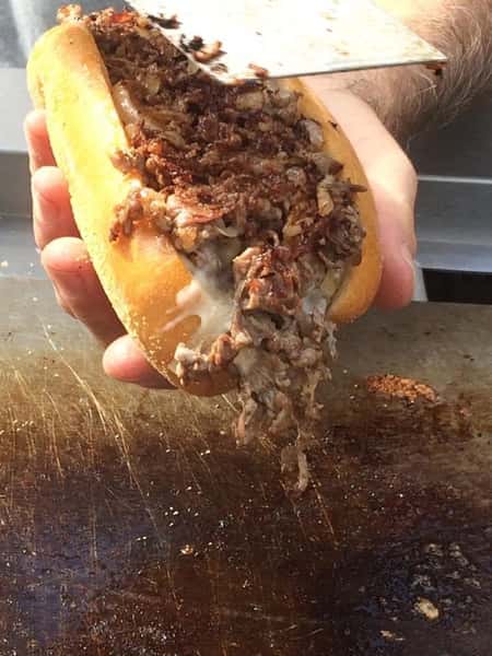 chef holding cheesesteak over a grill