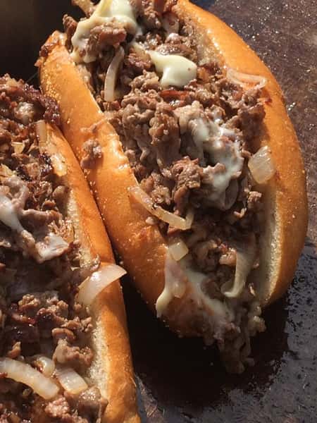 two cheesesteaks with onion on a grill