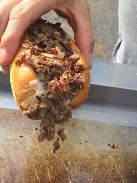 hand holding cheesesteak over grill