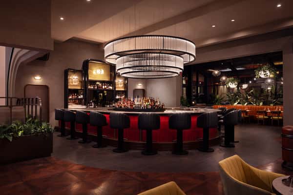 Modern upscale restaurant bar with red accents, black stools, and a large circular chandelier.