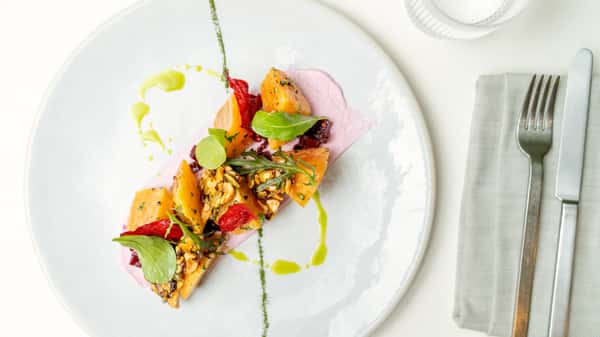 Colorful plated fine dining dish with vegetables, herbs, and sauce on a white plate