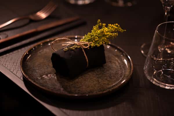 Elegant restaurant table setting with a black napkin, yellow flowers, and glassware in warm lighting.